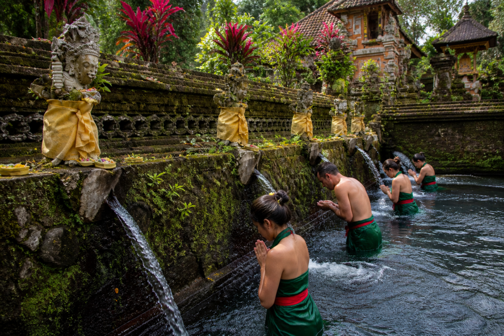 Women performing melukat purification ritual under water fountains at a quiet temple in Sebatu, Bali